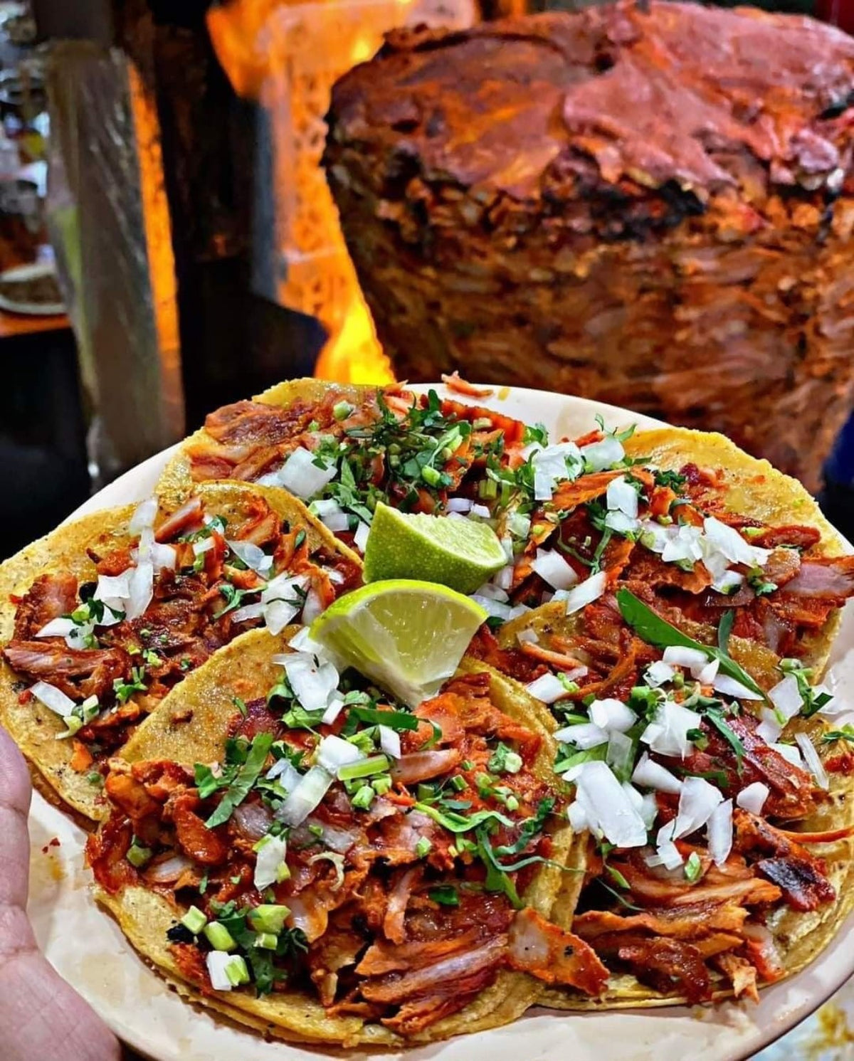 Tacos al pastor frente al trompo con cebolla, cilantro y limón